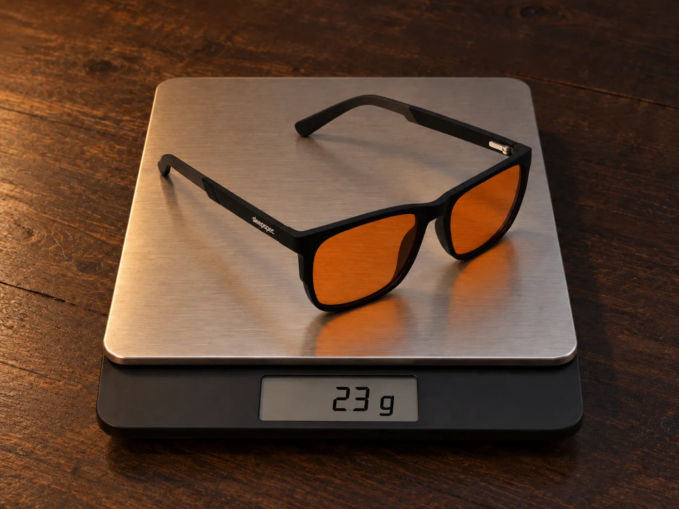 SleepSpec glasses resting on a kitchen scale on a wooden table. The display reads 23 g.