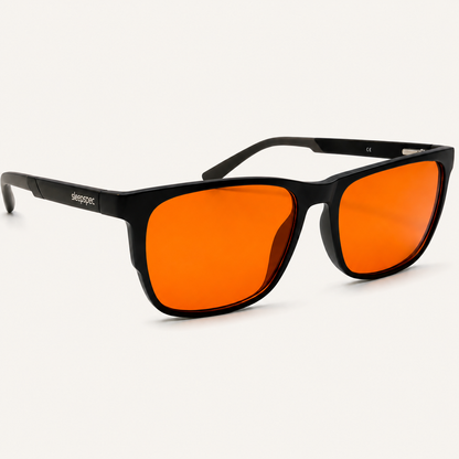 SleepSpec sleep glasses: black frame with deep-amber lenses, angled view on a light background