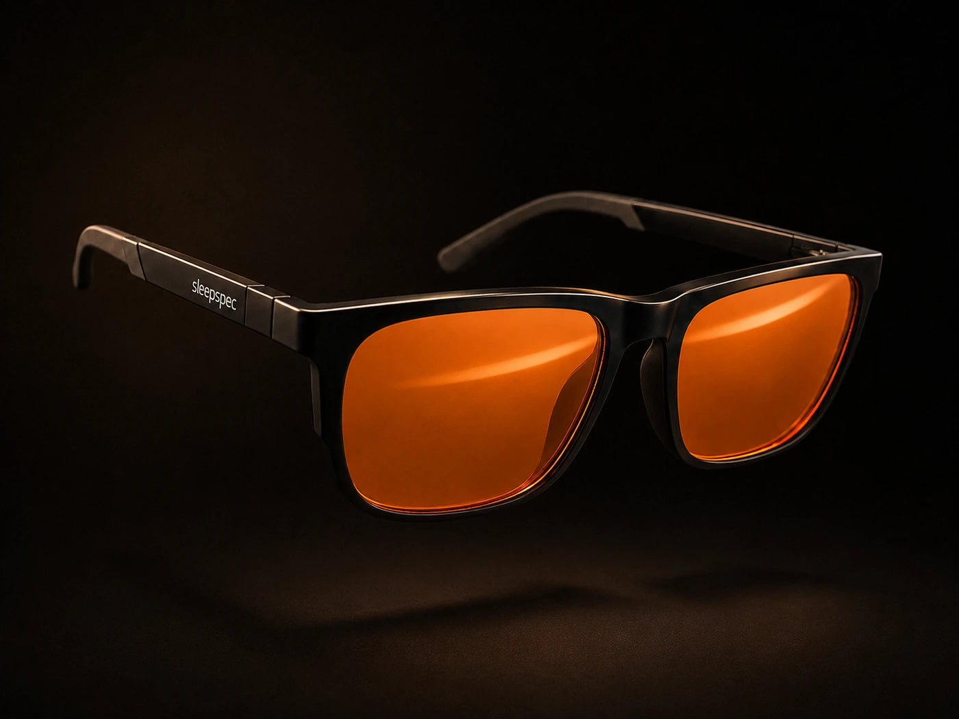 The SleepSpec frame suspended against a dark ground with the temples open, amber lenses lit and the hinge in view